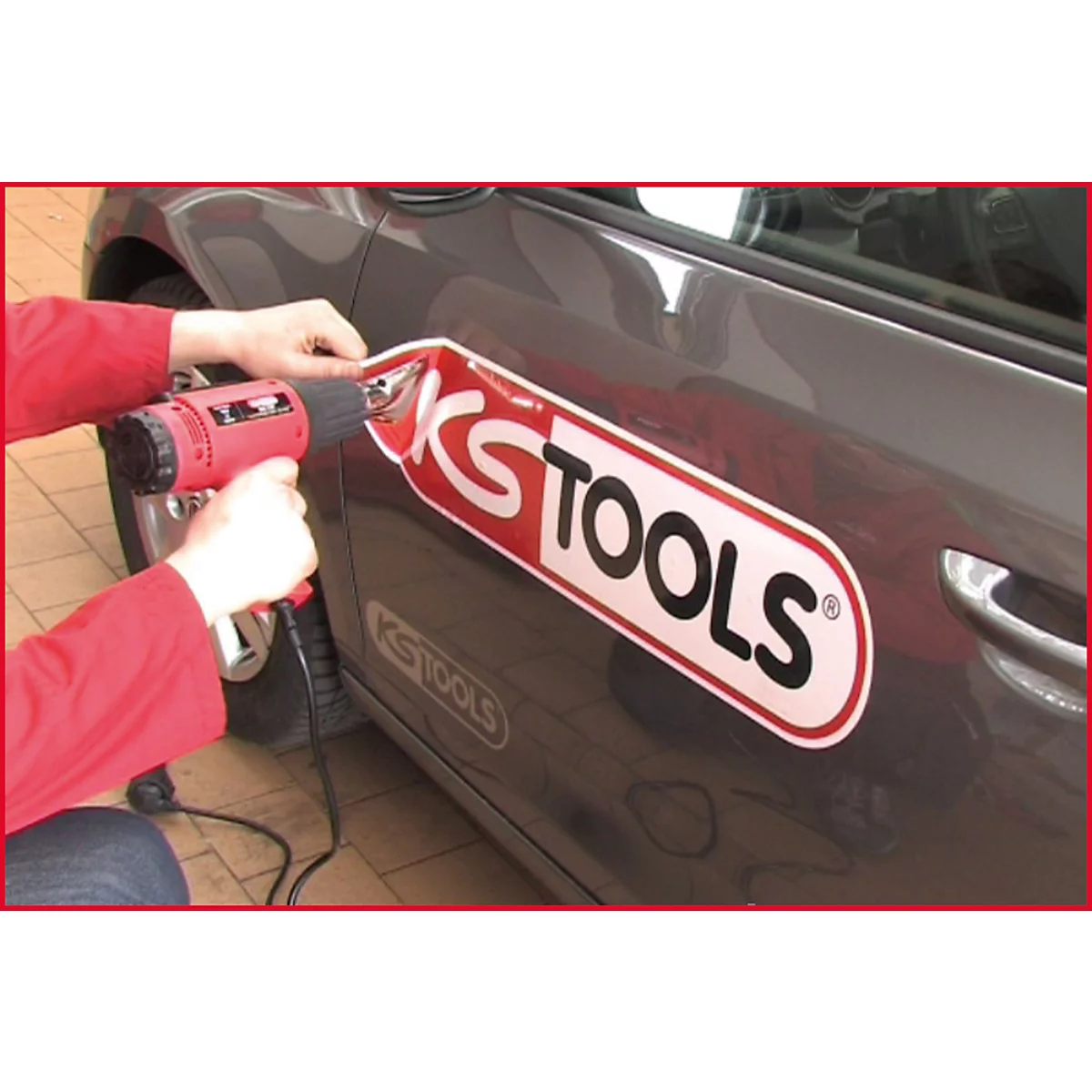 Person befestigt mit einem Heißluftföhn einen KS TOOLS-Aufkleber auf einem Autoteil.